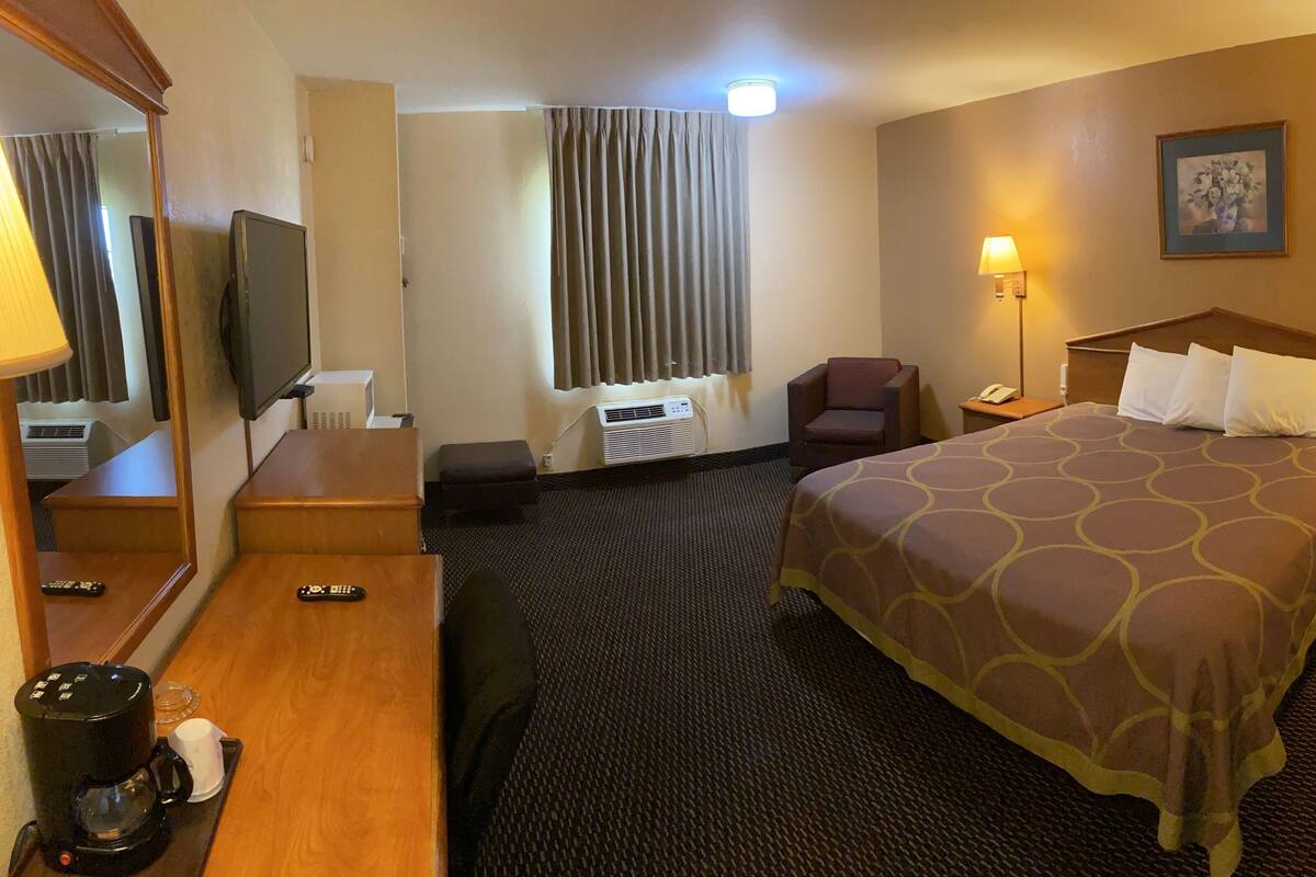 A hotel room with a bed, a chair, a desk with a coffee maker, a TV, and a window with curtains.