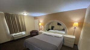 Ein Hotelzimmer mit Bett, Sessel, Schreibtisch mit Lampe und Spiegel.