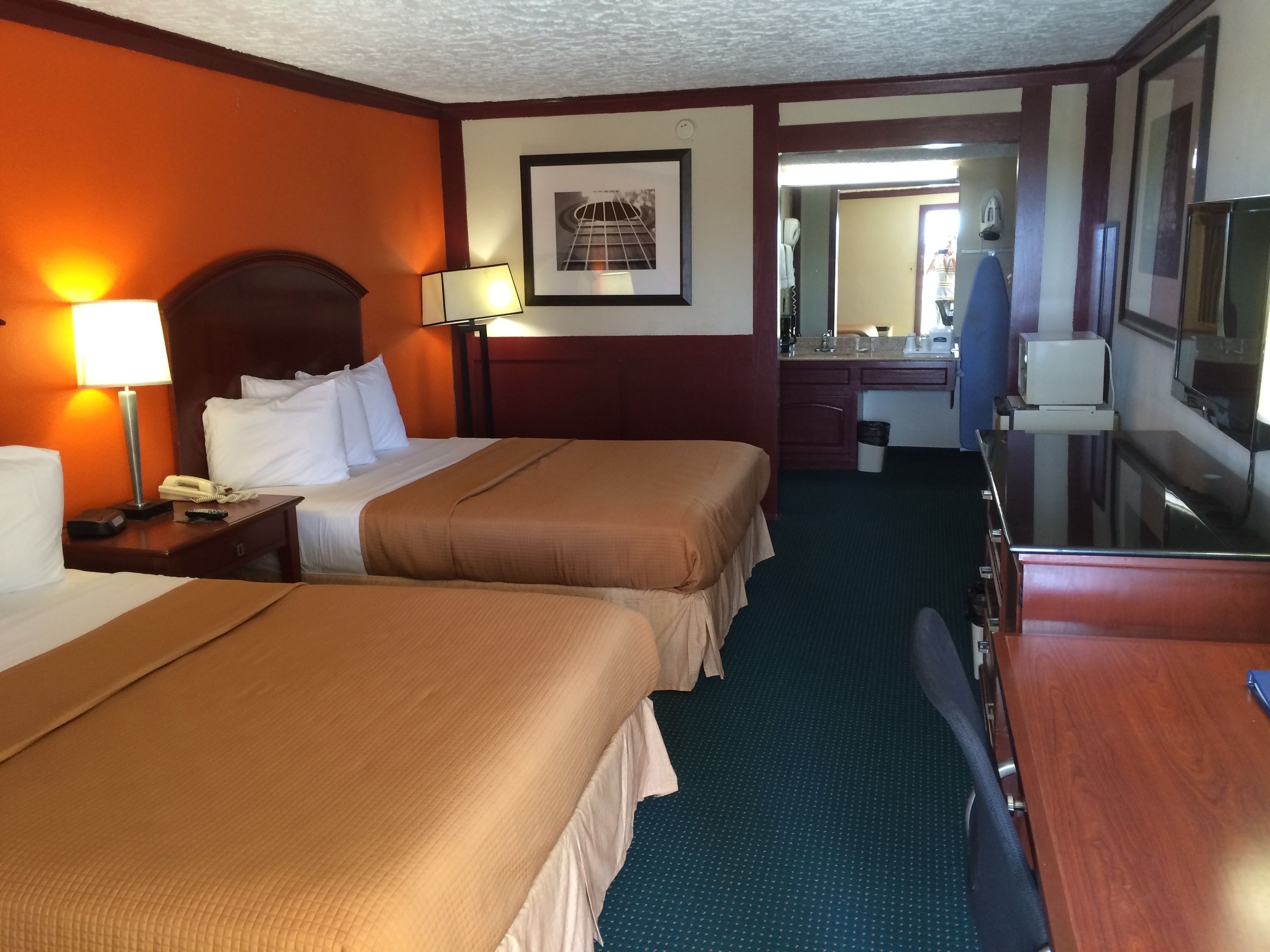 A hotel room with two beds, a desk, a mirror, a TV, and a bathroom visible through an open door.