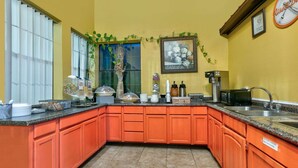A kitchen with orange cabinets, a coffee machine, and a clock on the wall.