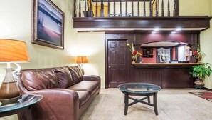 A lobby with a leather sofa, a glass coffee table, a wooden reception desk, and a staircase.