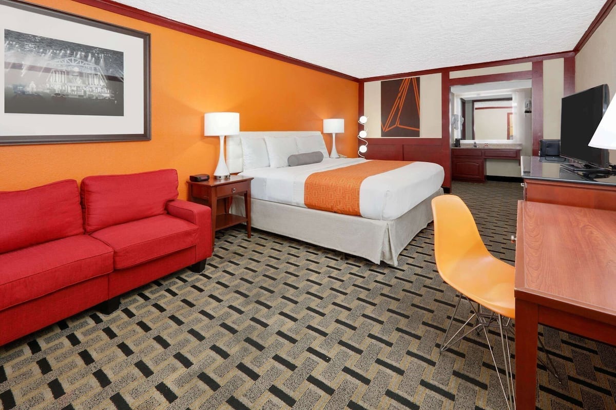 Una habitación de hotel con una cama, un sofá rojo, un escritorio y una silla.
