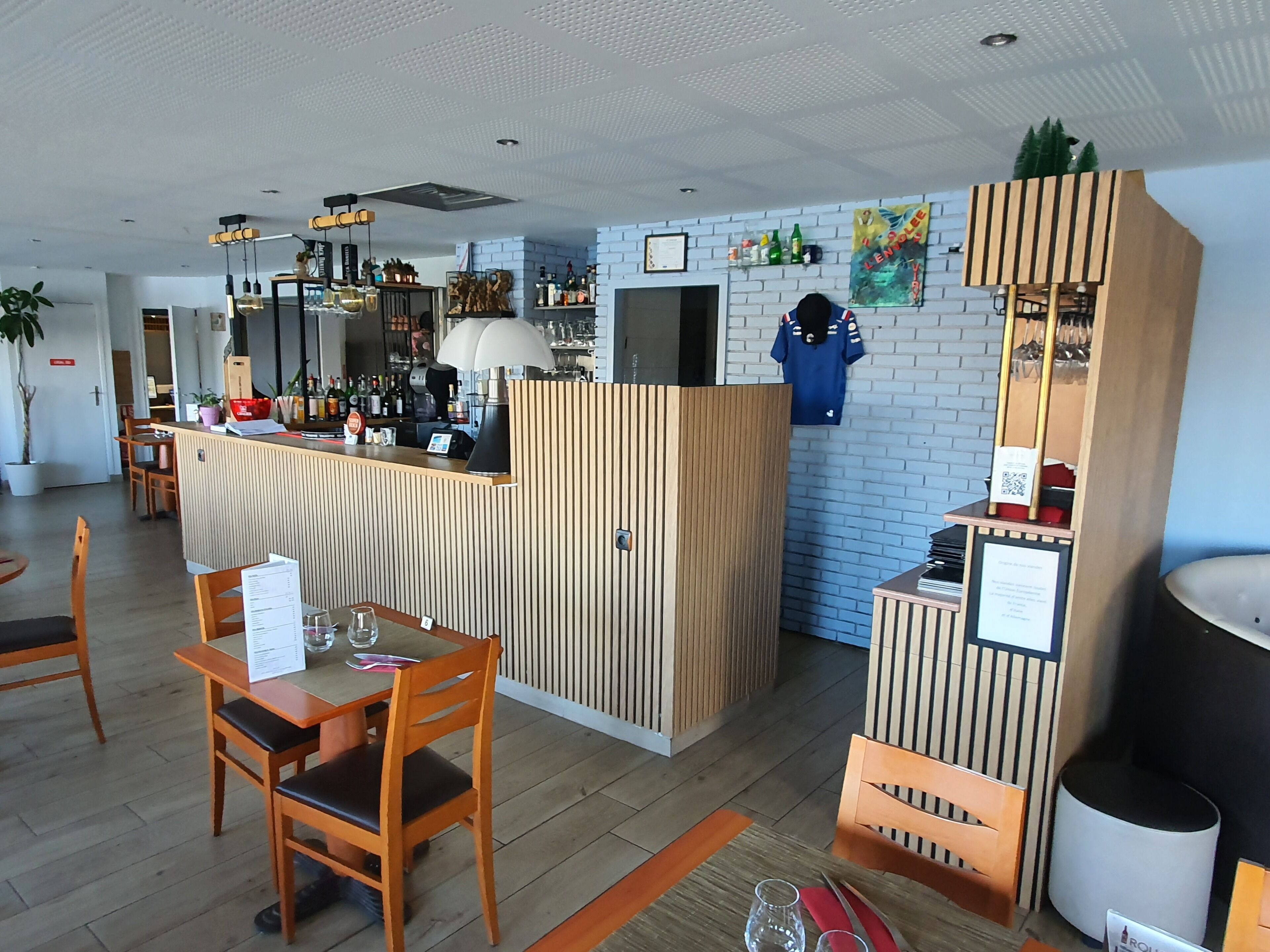Un espace bar moderne avec un comptoir en bois, des sièges et un mur en briques en arrière-plan.