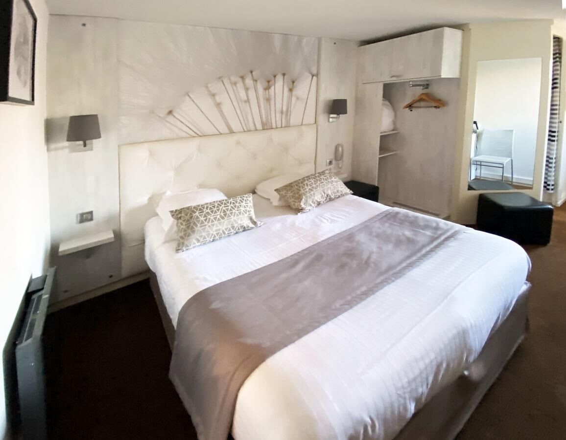 A hotel room with a large bed, a headboard with a unique design, a bedside table, and a wardrobe.