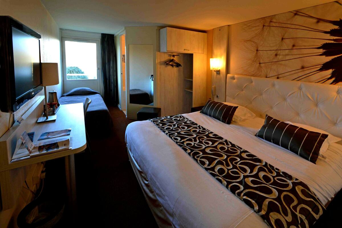 Ett hotellrum med en säng, ett skrivbord, en tv och ett fönster.