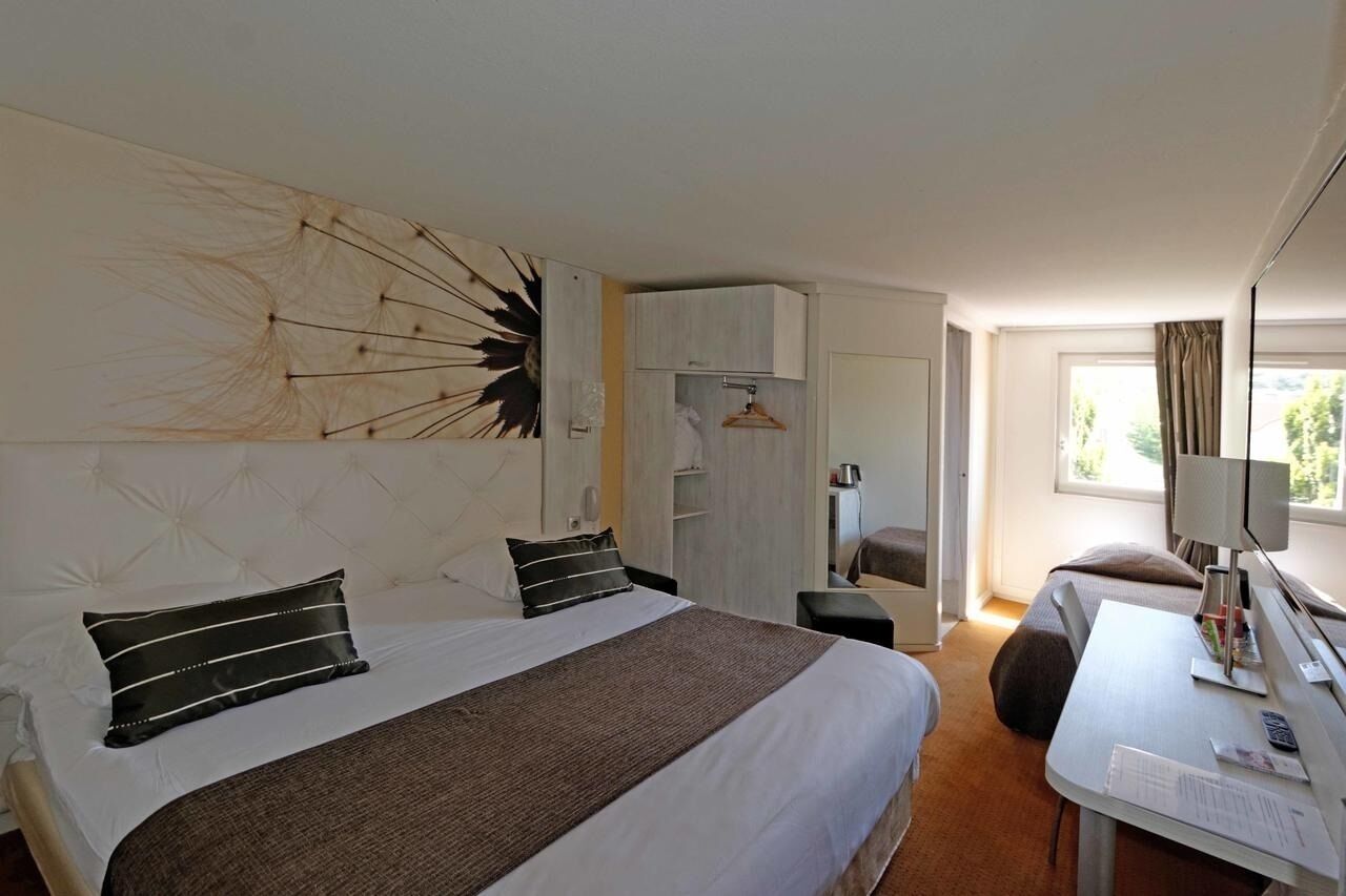A hotel room with a large bed, a desk, a chair, a wardrobe, and a window.