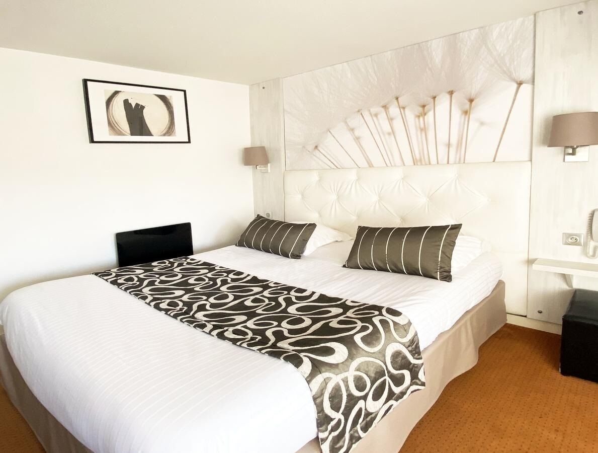 A hotel room with a large bed, a headboard with a fan design, a bedside lamp, and a framed picture on the wall.