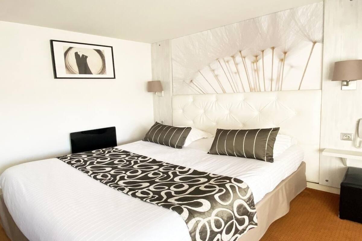 Ett hotellrum med en stor säng, en sänggavel med ett fläktmotiv, en sänglampa och en inramad tavla på väggen.