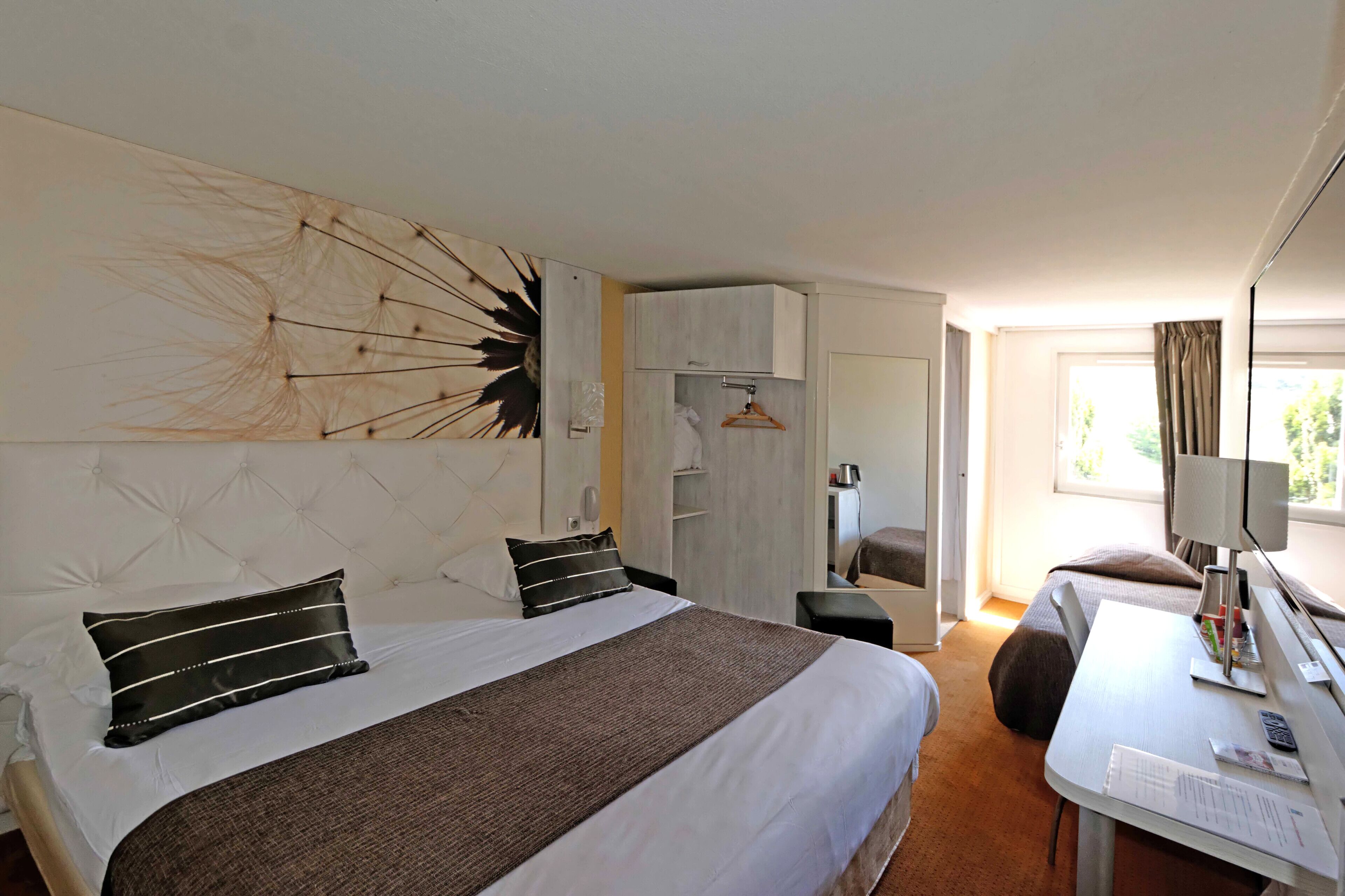 A modern hotel room with a large bed, a desk, and a wardrobe.
