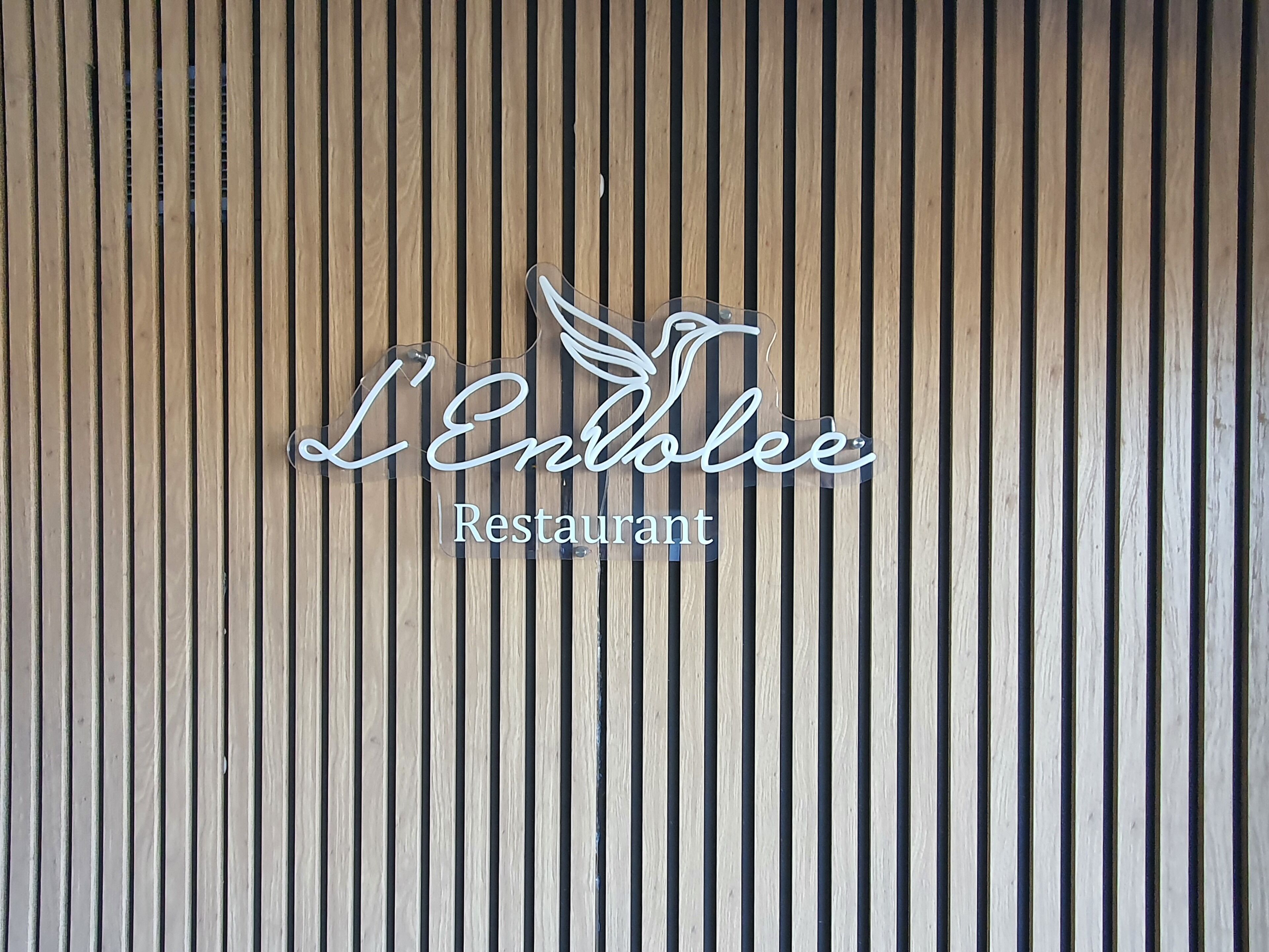A vertical wooden slat wall with a sign that reads 'L'Ennolee Restaurant.'