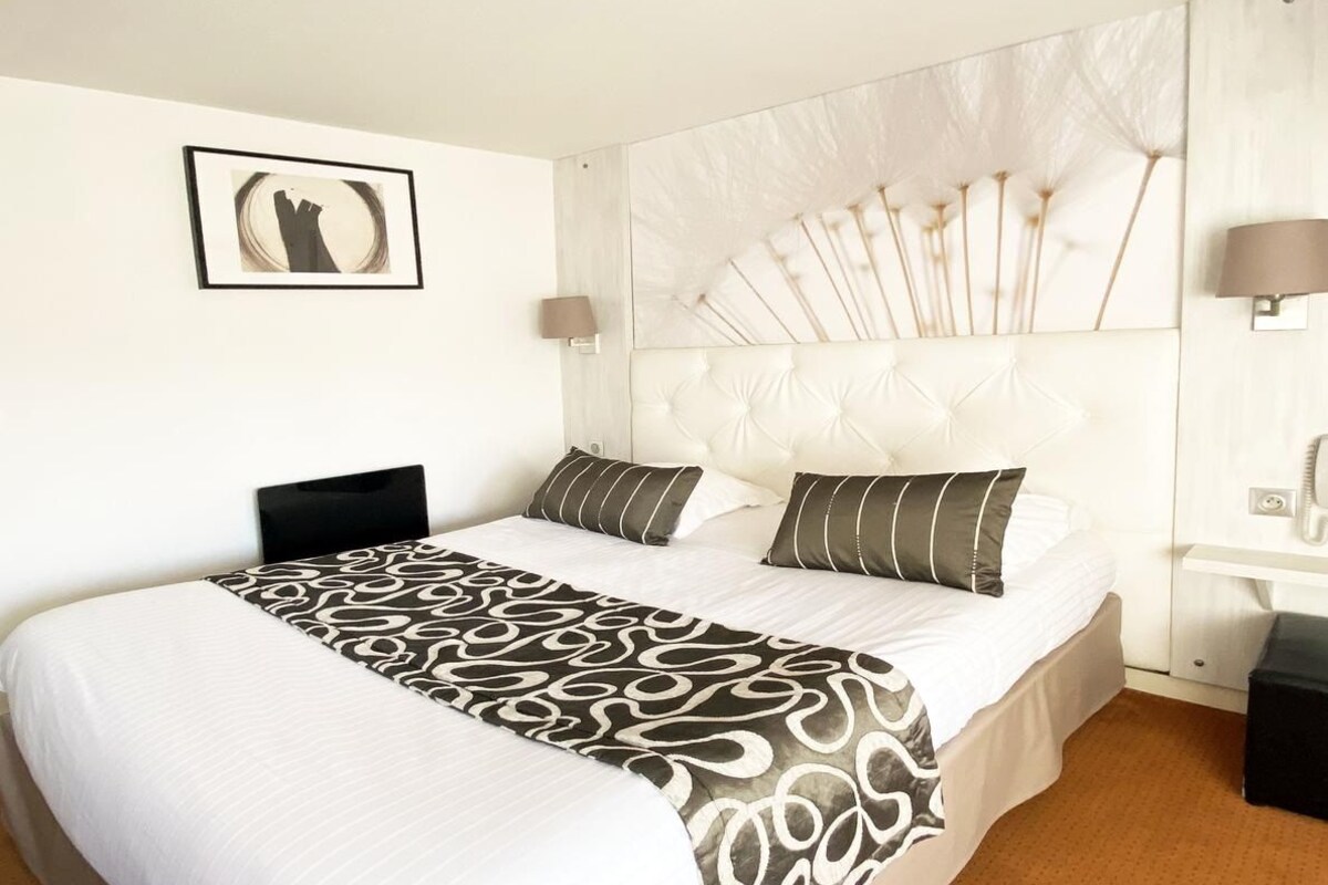 Une chambre d’hôtel avec un grand lit, une tête de lit ornée d’un motif en forme de ventilateur, une lampe de chevet et un tableau encadré au mur.