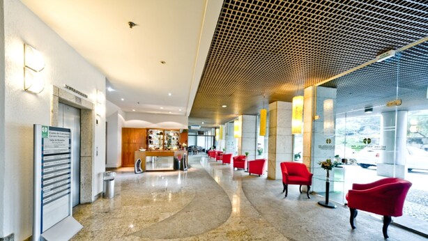 Een ruime lobby met een gebogen marmeren vloer, rode zitplaatsen, een receptiebalie en een modern plafondontwerp.
