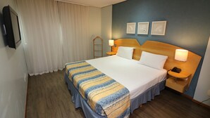 Een hotelkamer met een groot bed, een nachtkastje met een lamp, een telefoon en een aan de muur bevestigde televisie.