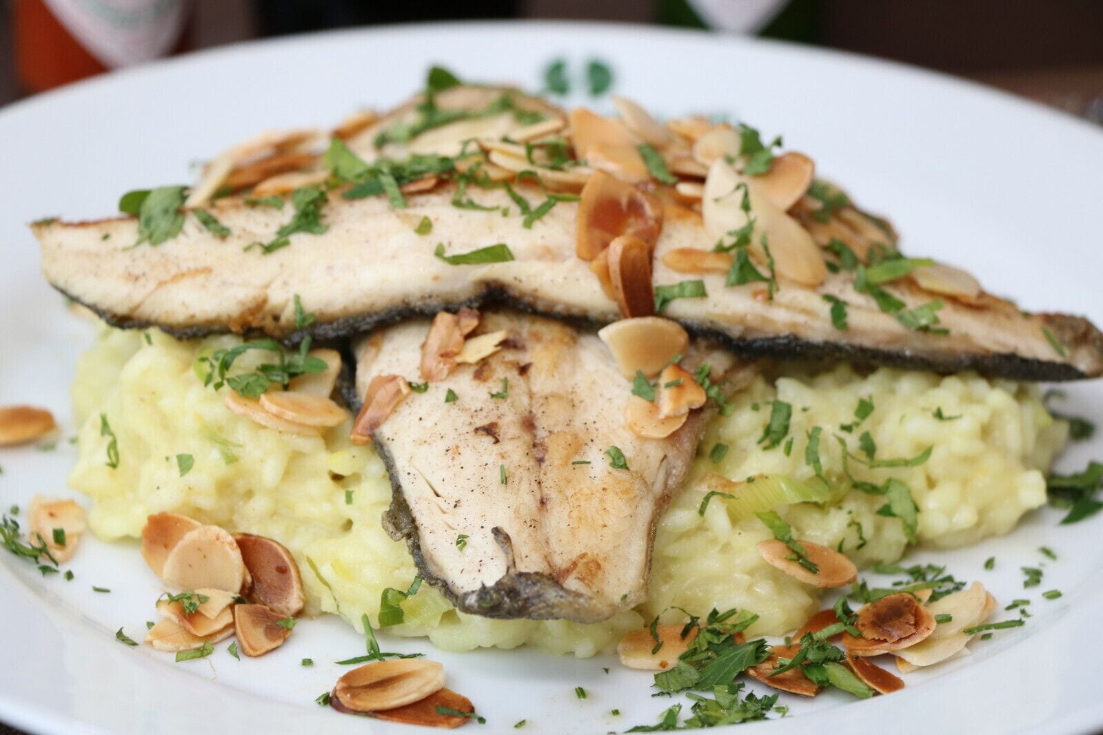 A plate of food with sliced chicken and mushrooms on top of mashed potatoes, garnished with herbs and nuts.
