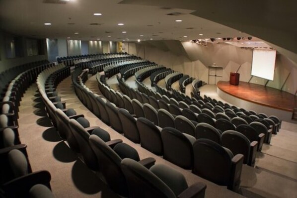 Un gran auditorio con filas de asientos, un escenario y una pantalla de proyección.