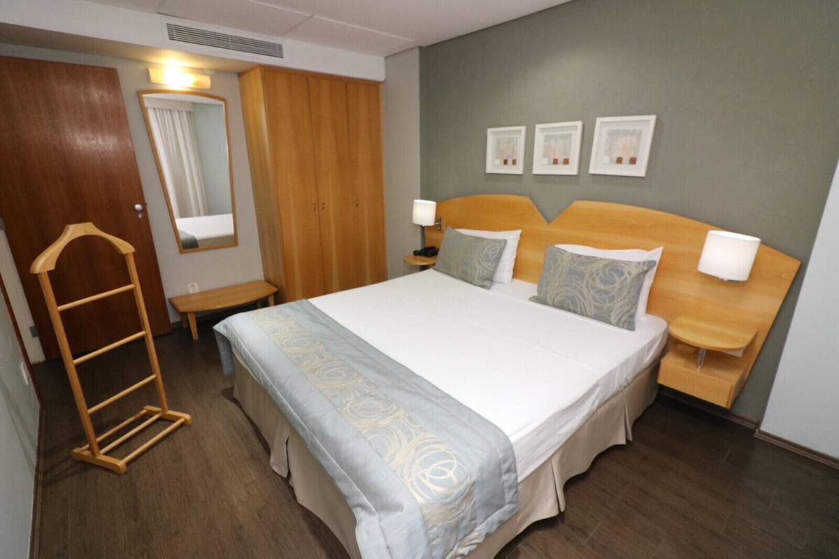 Ein Hotelzimmer mit einem großen Bett, einem Holzschrank, Nachttischen mit Lampen und drei gerahmten Bildern an der Wand.
