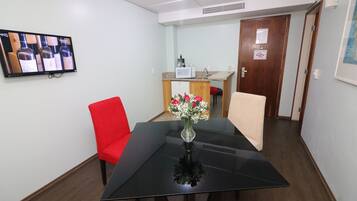 Un salón de conferencias con una mesa negra, sillas rojas y beige, un jarrón con flores y una televisión en la pared.
