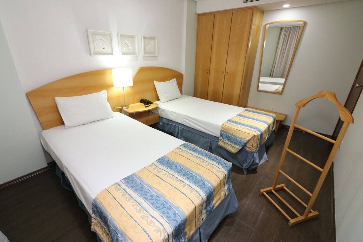 Ein Hotelzimmer mit zwei Betten, einem Holzschrank, einem Nachttisch mit Lampe, einem Spiegel und einer Holzleiter.