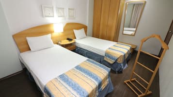 Et hotelværelse med to senge, en træskab, et sengebord med lampe, et spejl og en træstige.