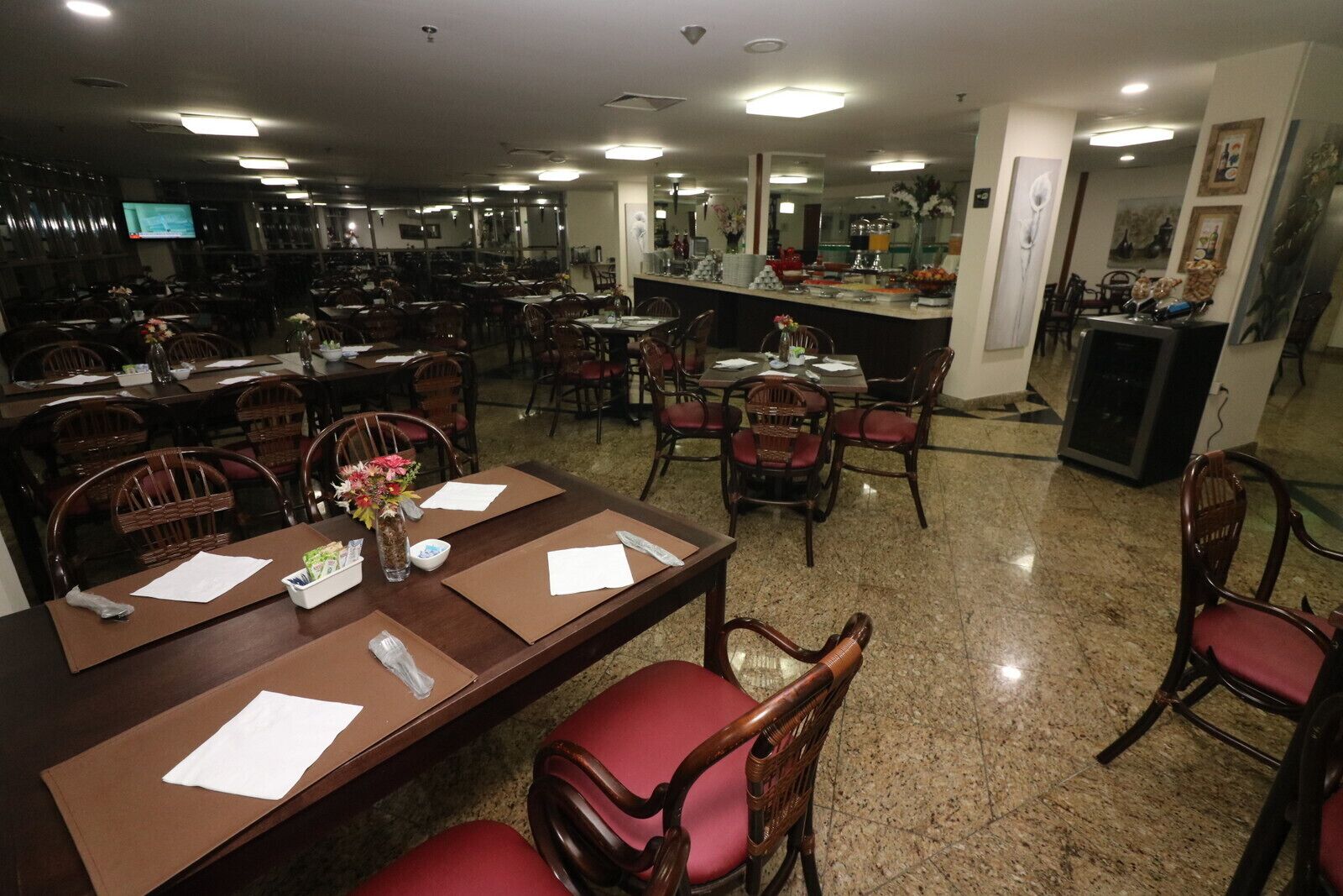 A spacious dining area with multiple tables and chairs, equipped with paper placemats and a vase with flowers.