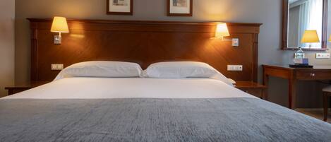 Et hotelværelse med en stor seng, to sengeborde med lamper, et træhovedgærde og to billeder i rammer på væggen.