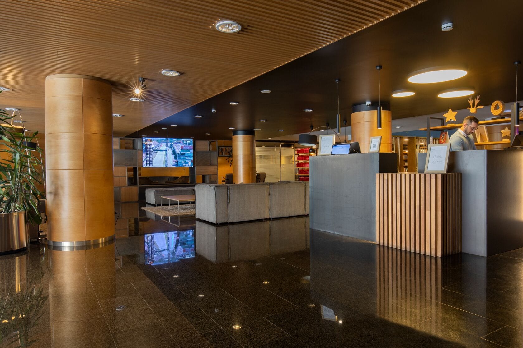 A modern lobby with a reception desk, seating area, and a large screen displaying a cityscape.