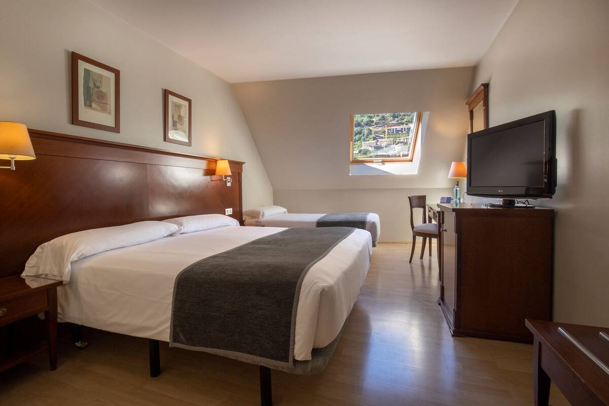 Une chambre d’hôtel avec un grand lit, un bureau avec une chaise, une télévision et des œuvres d’art encadrées accrochées aux murs.