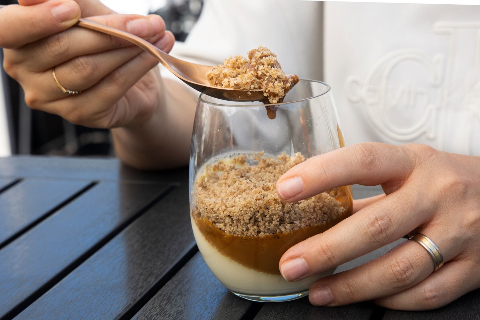 Una persona sosteniendo una cuchara con un postre, posiblemente un pudín, en un bol de vidrio.