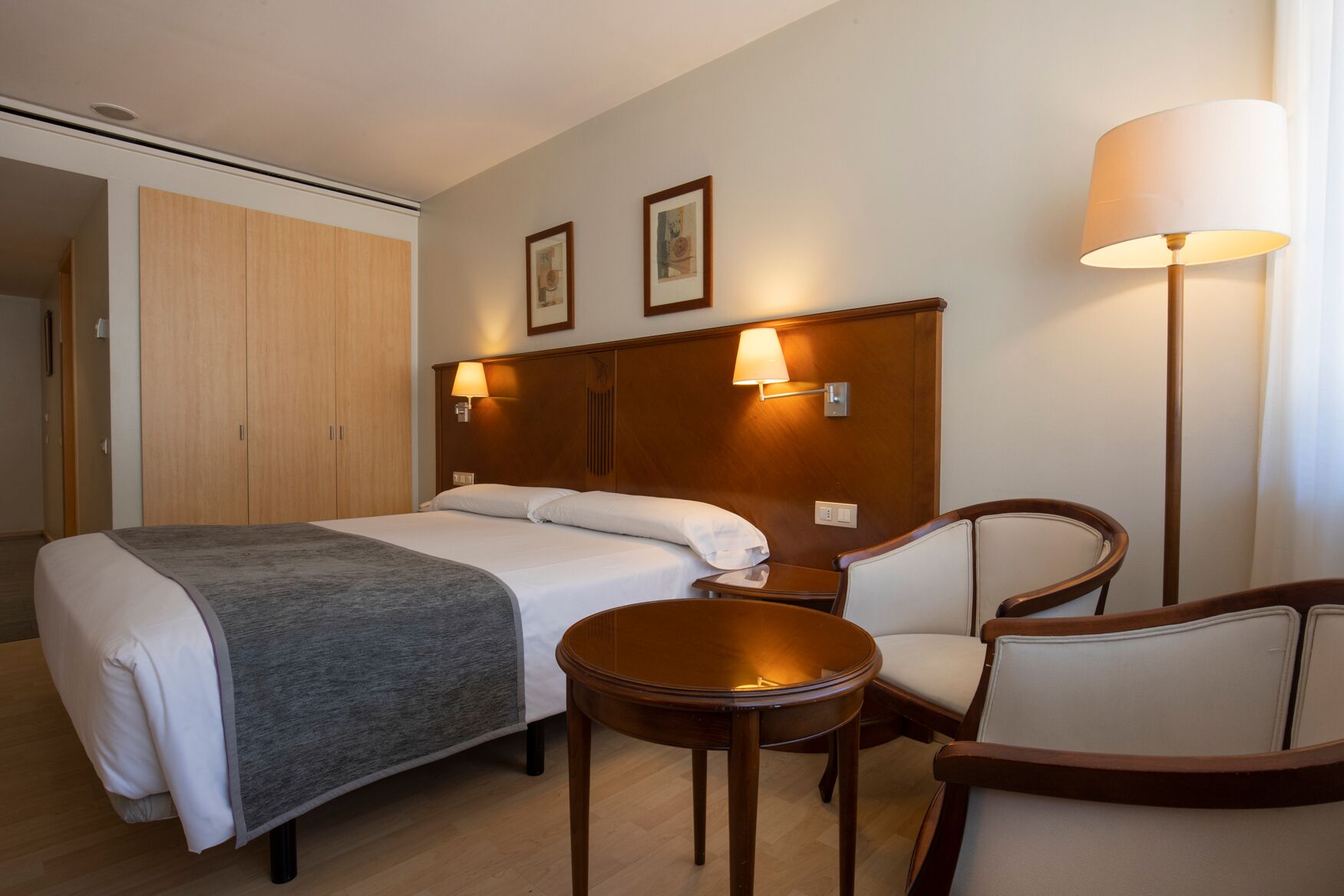 Una habitación de hotel con cama, mesitas de noche, una silla, lámpara y armario.