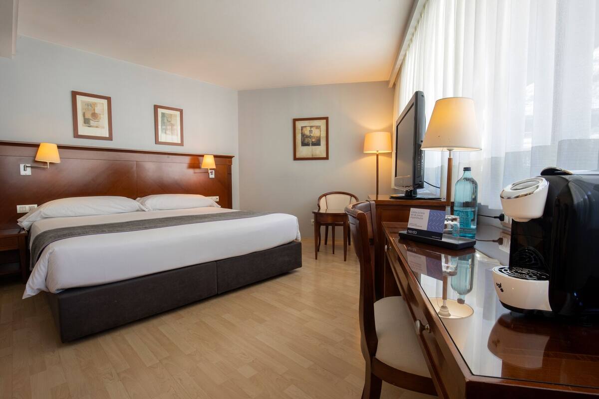 Une chambre d’hôtel comprenant un lit, des lampes de chevet, un bureau avec une machine à café, une télévision et une chaise.