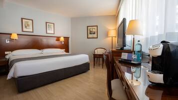Habitación de hotel con cama, lámparas de noche, escritorio con cafetera, televisión y una silla.