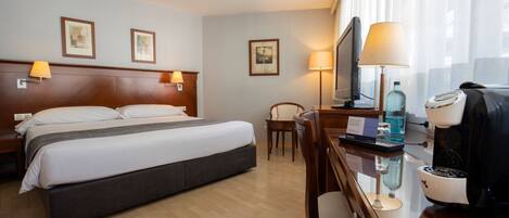 Habitación de hotel con cama, lámparas de noche, escritorio con cafetera, televisión y una silla.