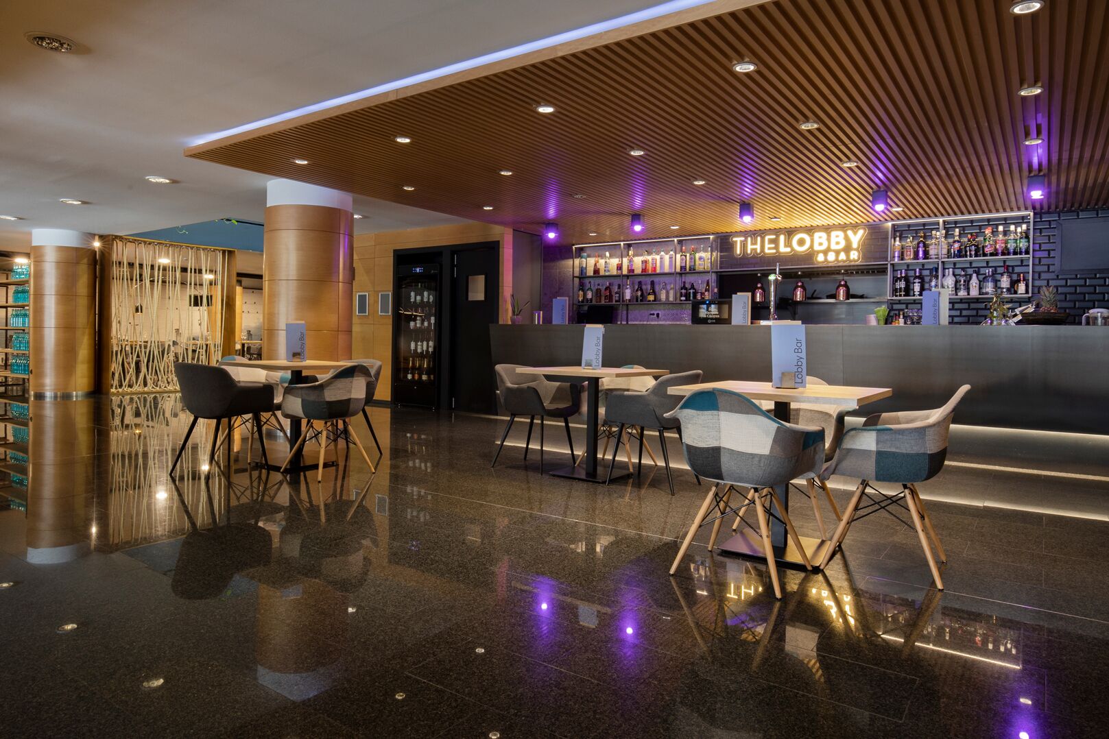 Un vestíbulo con una zona de bar llamada 'THELOBBY BAR', arreglos de asientos y un diseño moderno con detalles de madera.