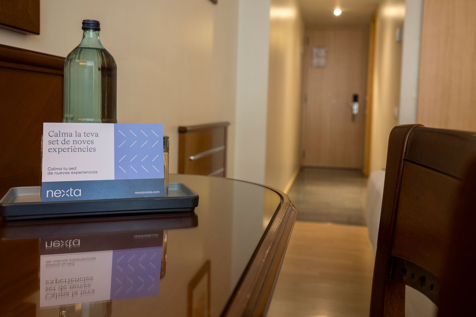 A hotel reception desk with a glass top, a bottle, and a sign with text and a website address.