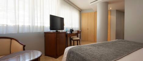 A hotel room with a bed, a desk, a chair, a television, and a wardrobe.