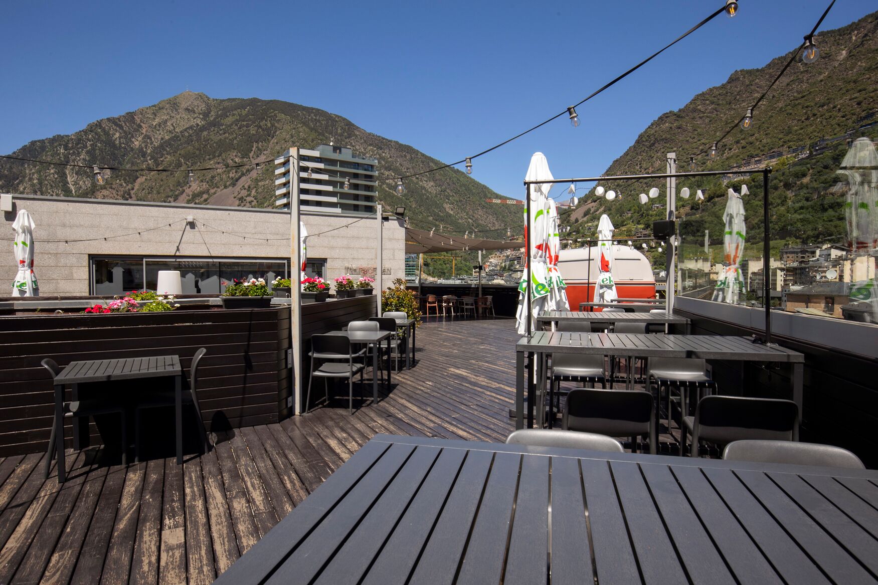 An outdoor terrace with tables and chairs, a view of a mountain, and a building in the background.