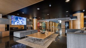 Een moderne lobby met een grote televisie, zithoeken en een trap.