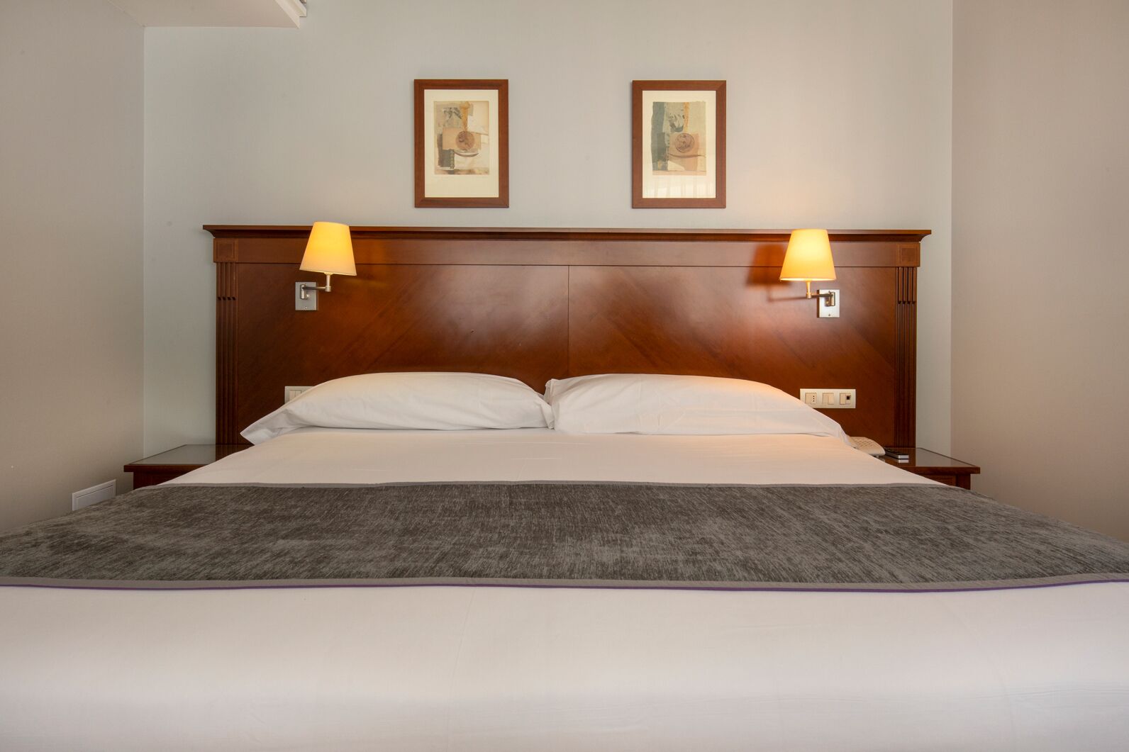 Una habitación de hotel con una cama grande, dos lámparas de noche y dos cuadros en la pared.