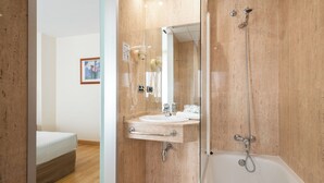 A modern bathroom with a bathtub, a sink with a mirror, and a hairdryer. -  Hotel Longoria Plaza by Pandora Hoteles (Oviedo)