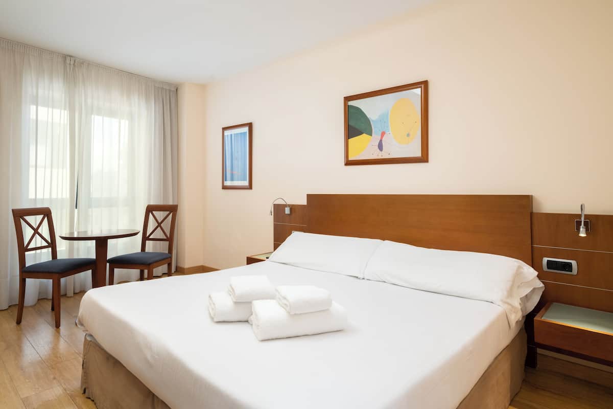 A hotel room with a large bed, two chairs, a small table, and artwork on the walls.