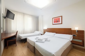 Hotellihuone, jossa on kaksi sänkyä, työpöytä, tuoli, televisio ja seinällä kehystetty taulu.