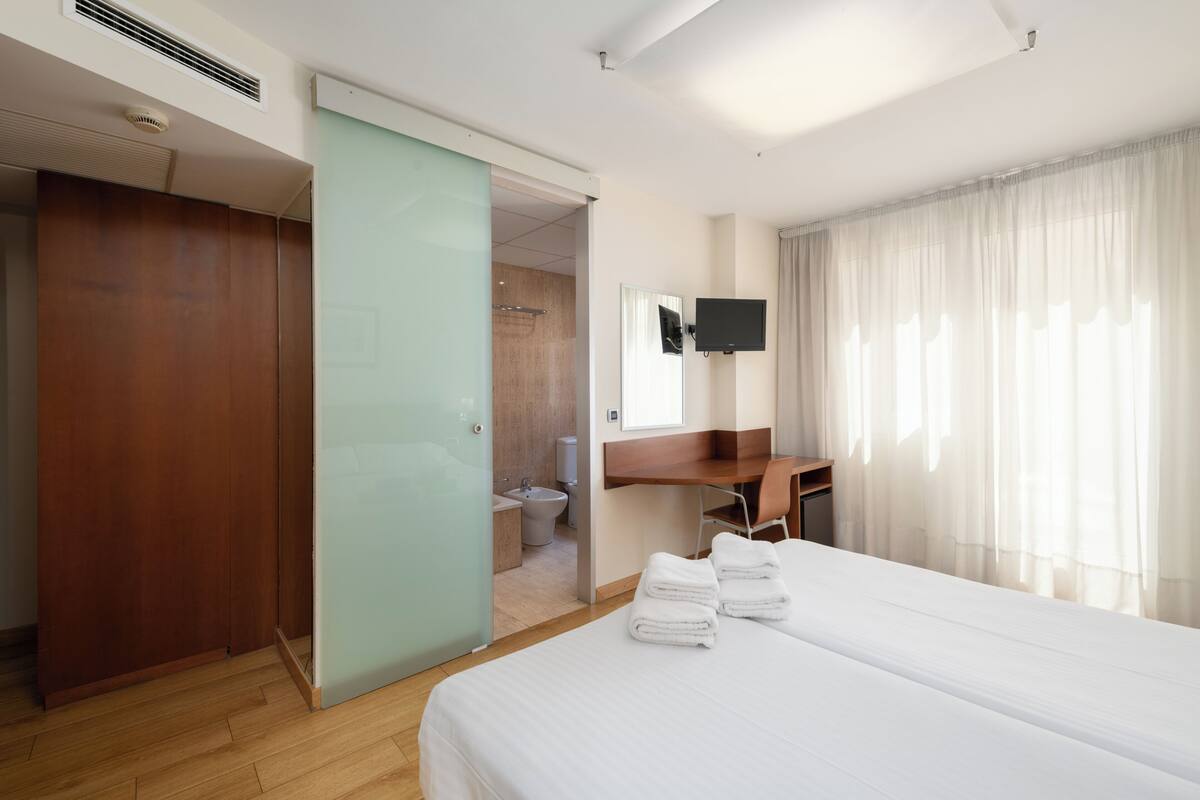 A hotel room with a bed, a desk, a television, and a bathroom visible through an open door.
