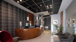 A reception area with a wooden reception desk, a red chair, and a seating area with grey sofas. -  Hotel Longoria Plaza by Pandora Hoteles (Oviedo)