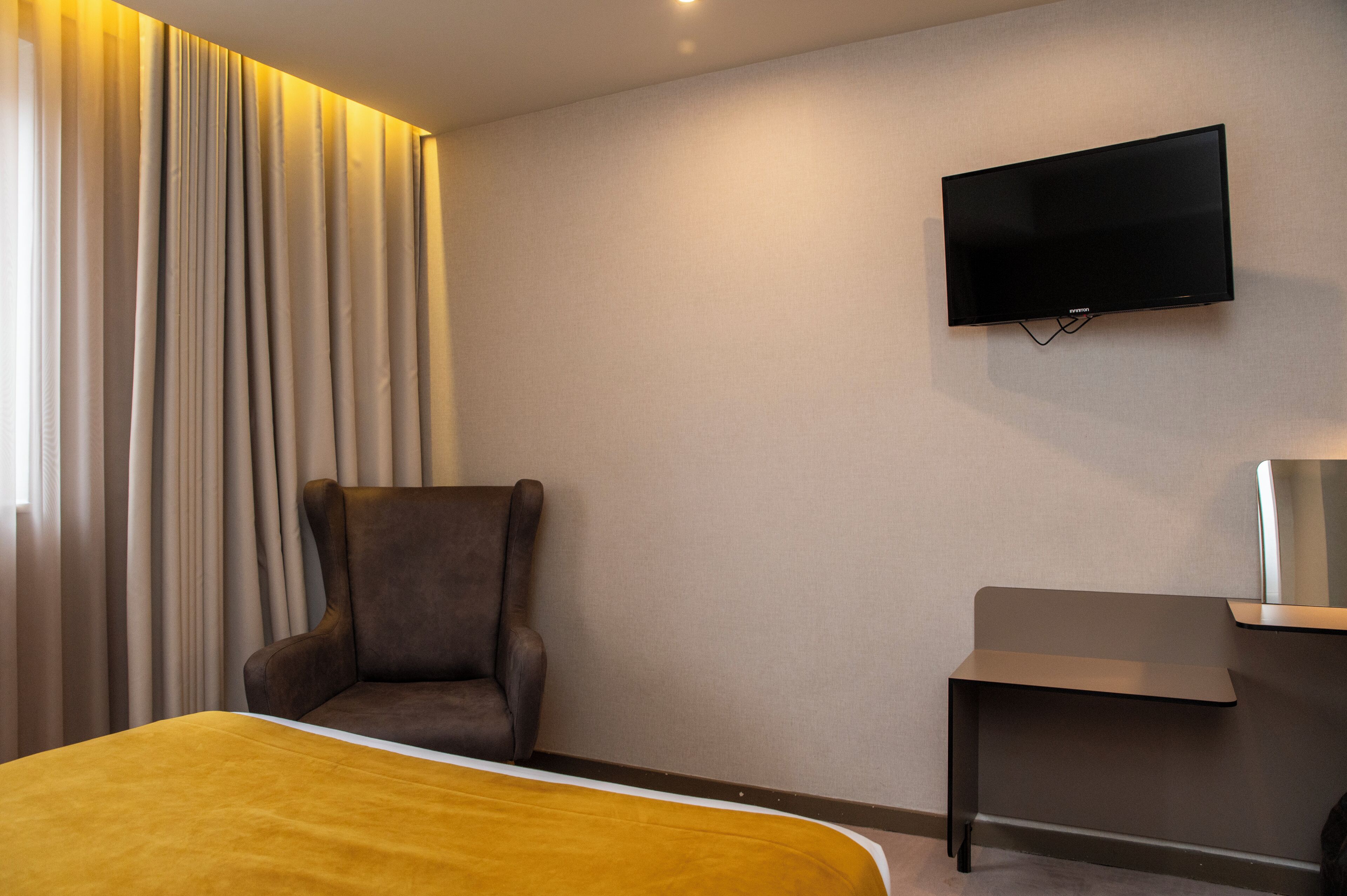 Una habitación de hotel con cama, una silla, un televisor montado en la pared y una mesita.