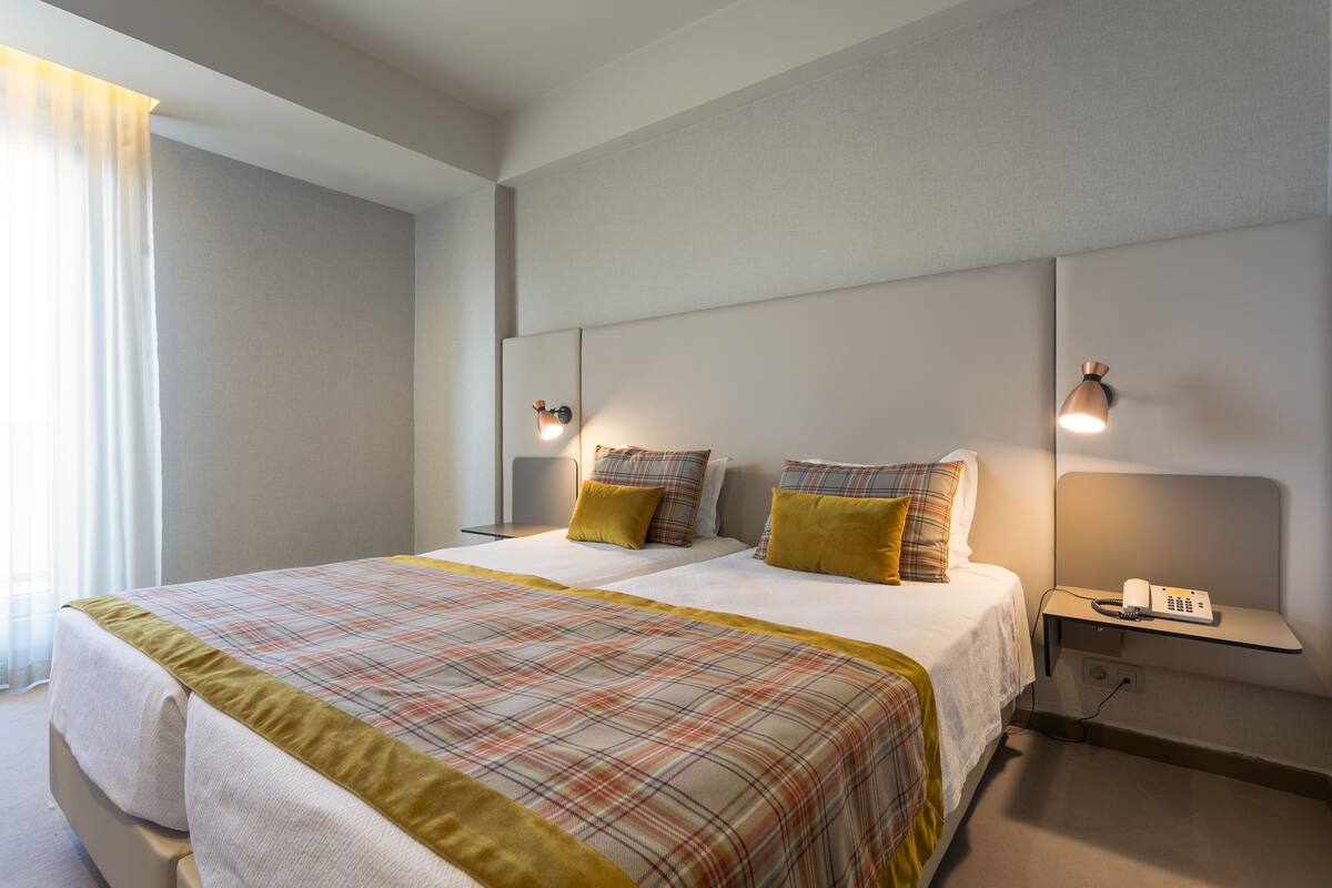 A double bed with a plaid bedspread, two bedside lamps, and a bedside table with a phone and remote control.