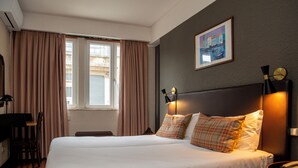 Une chambre d’hôtel avec un grand lit, un bureau avec une chaise, une fenêtre avec des rideaux et une horloge fixée au mur.