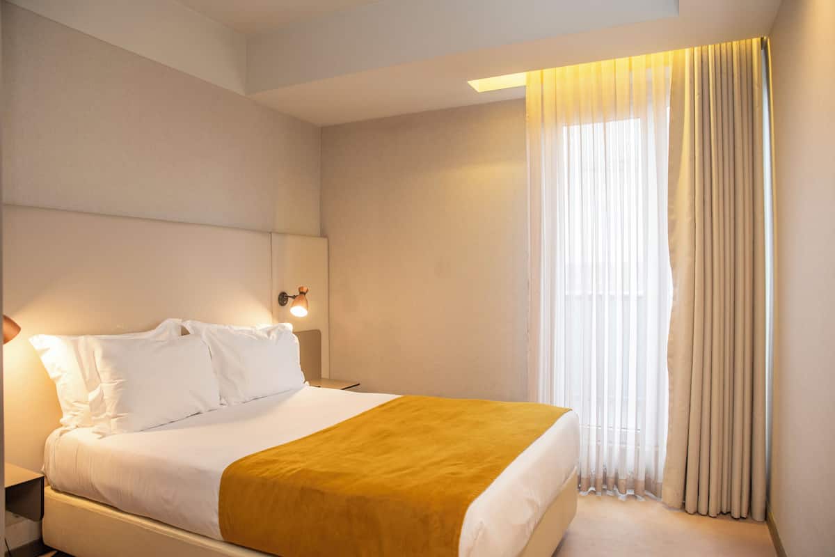 A hotel room with a bed, a nightstand, a lamp, and a window with curtains.