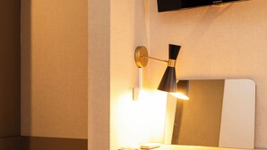 Une chambre d’hôtel moderne dotée d’un téléviseur à écran plat fixé au mur, d’une table de chevet avec une lampe et d’un grand miroir.