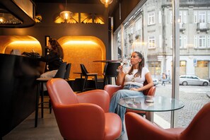 Un café moderno con sillas de cuero y una mesa de vidrio, una mujer sosteniendo un vaso, y otra mujer en la barra.