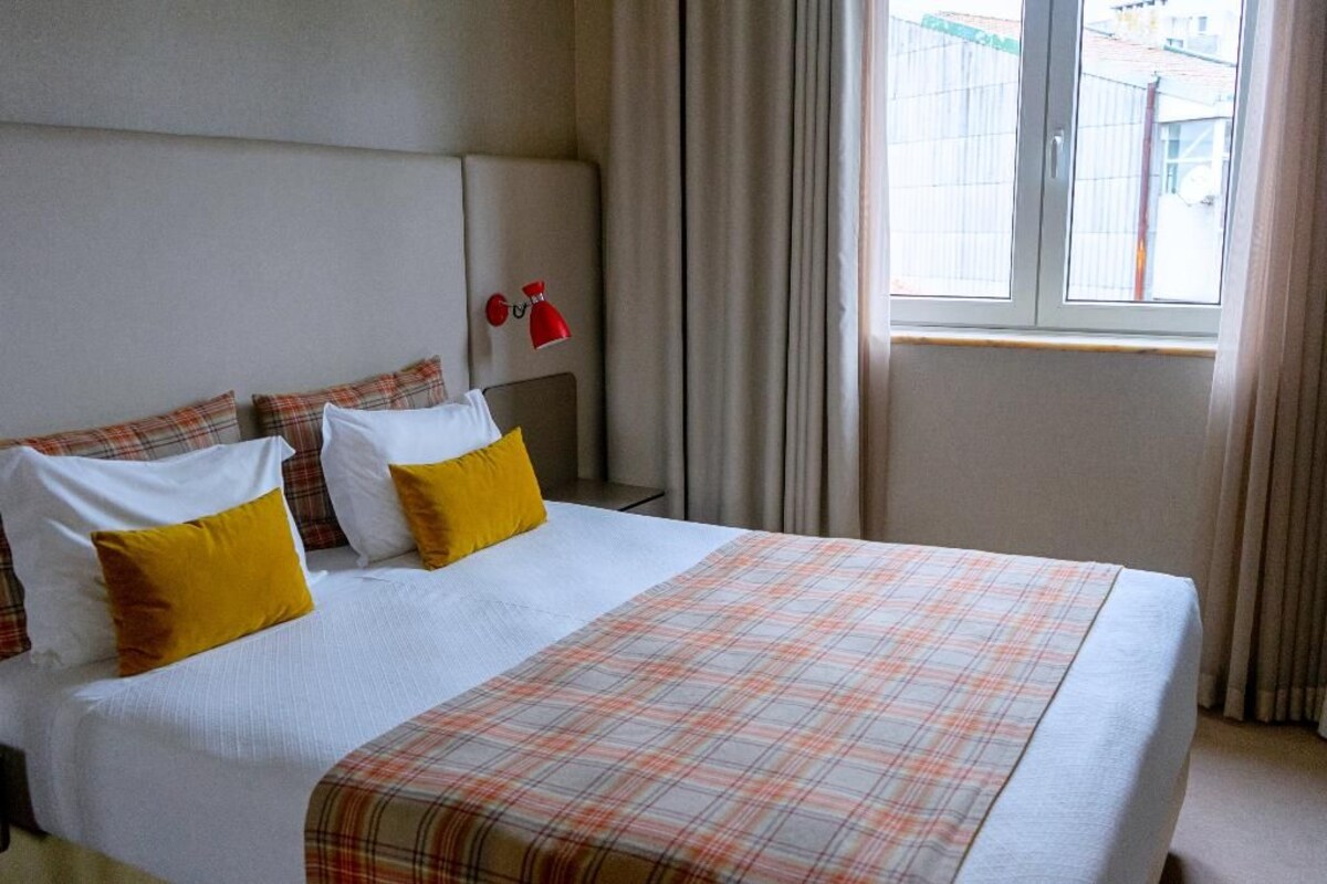 A hotel room with a bed, curtains, and a window.